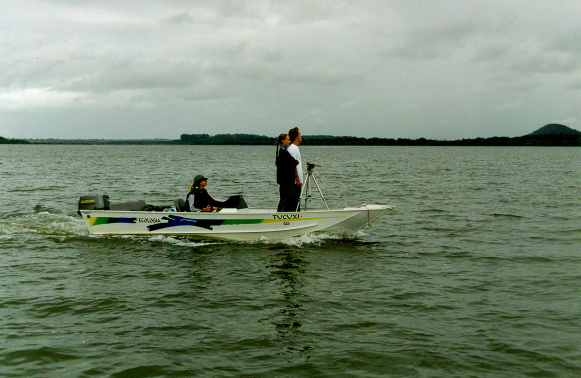 Três pesquisadores à bordo de uma pequena embarcação com um telêmetro em campo para estimativa de abundância de toninhas na Baía Babitonga (SC) em 2003