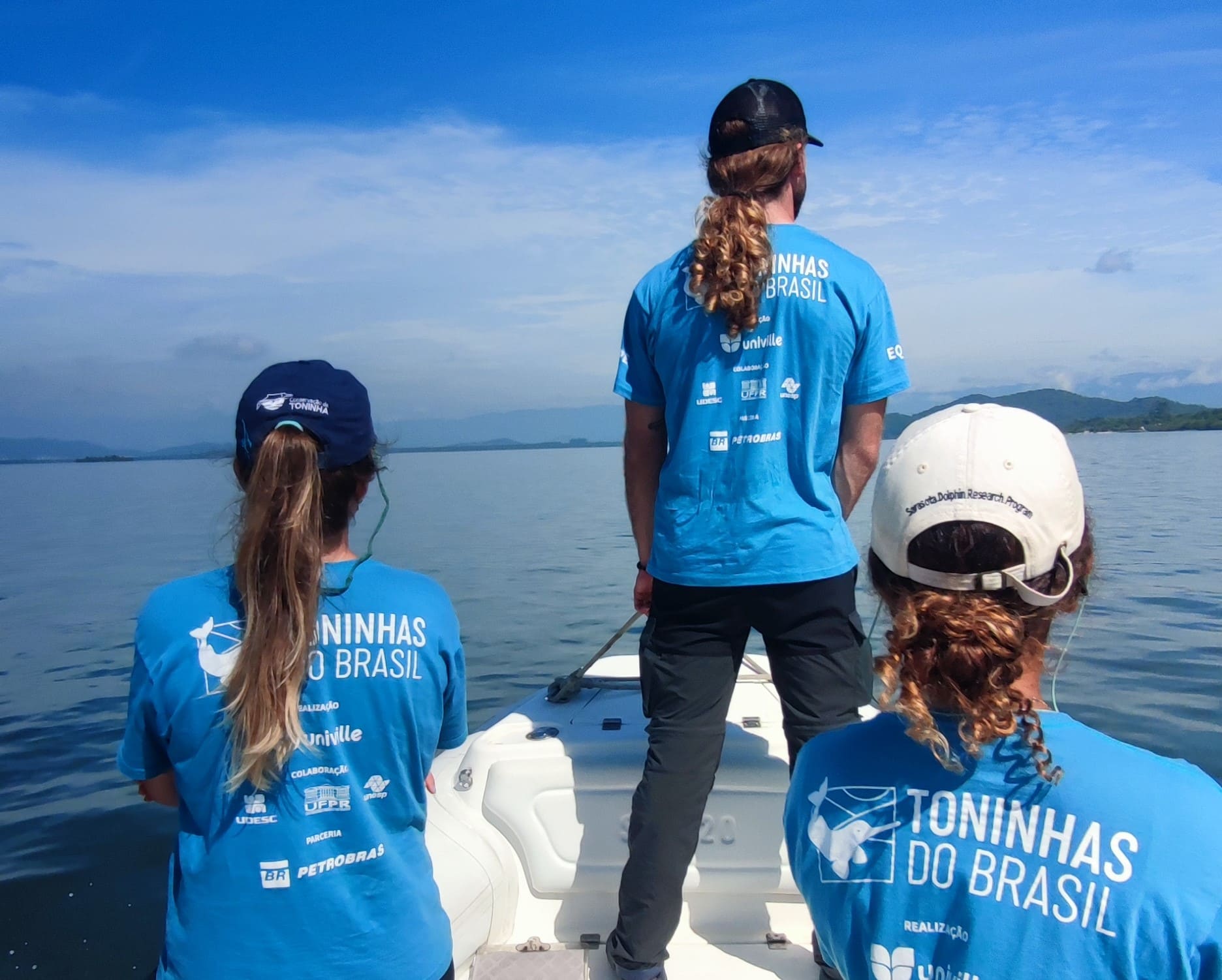 Três pesquisadores do Toninhas do Brasil a bordo de embarcação durante o monitoramento visual de toninhas na Baía Babitonga.