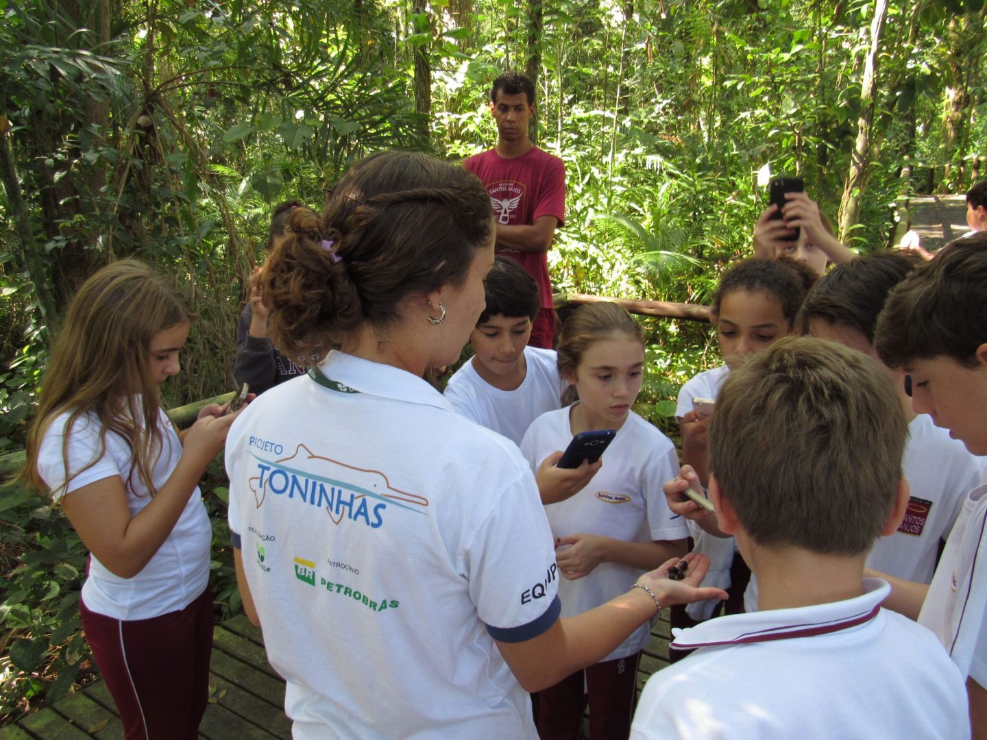 Educadora ambiental do Projeto Toninhas do Brasil mostra para um pequeno grupo de crianças uma semente de palmito juçara em uma das trilhas ecológicas do Projeto.